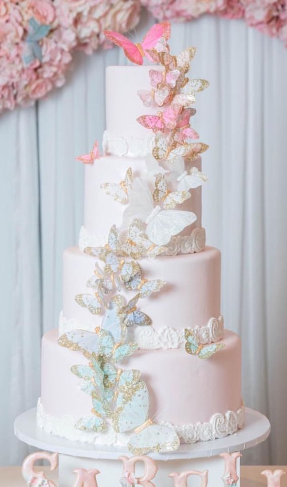 a light pink wedding cake with white lace, blue and gold butterflies plus white and pink ones on top is very chic