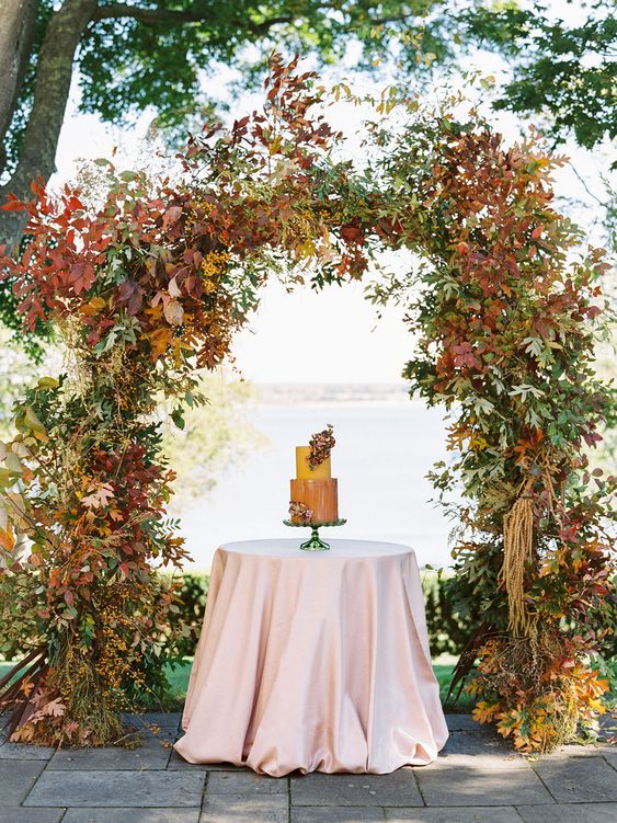 a lush fall leaf wedding arch covered with colorful and usual foliage is a lovely idea for a fall celebration