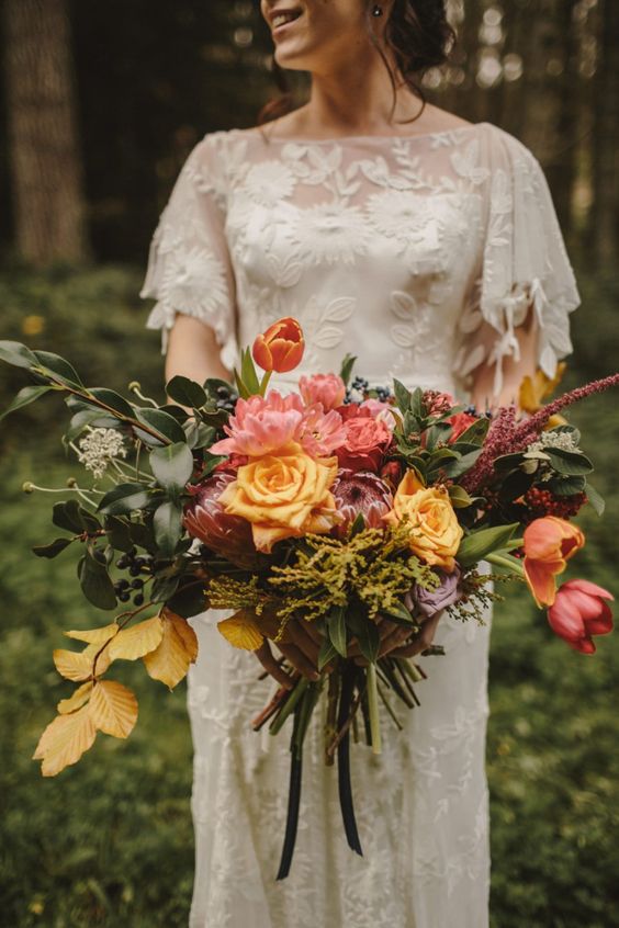 a lush fall wedding bouquet of pink and yellow blooms, tulips, roses and king proteas, greenery and bold fall foliage