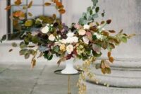 a lush fall wedding centerpiece with white blooms and fall leaves looks very natural and soft