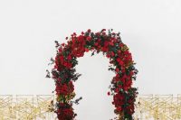 a lush red rose and greenery wedding arch with gold and white chairs make up a refined ceremony space