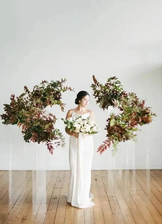 a minimalist wedding altar of acrylic stands with bold leaves and greenery is a beautiful idea for a fall minimalist wedding