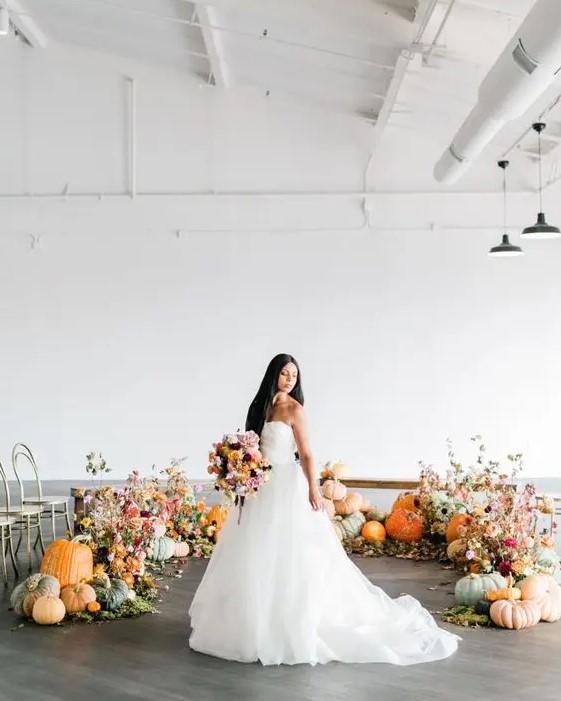a modern rustic fall wedding altar with pumpkins, greenery and bold fall leaves is beautiful idea to steal