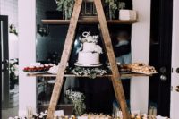 a modern rustic wedding dessert bar of a ladder, white blooms and greenery and lots of desserts