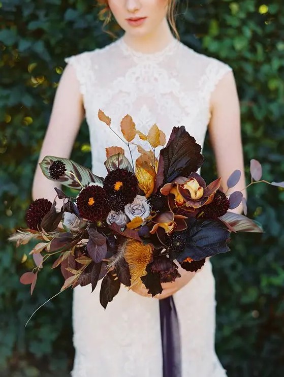 a moody and luxurious fall wedding bouquet with dark leaves, blooms, touches of mustard and rust, dried leaves and some herbs