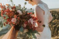 a moody lush bridal bouquet with rust, red, burgundy, pink blooms and textural greenery and colored ribbons