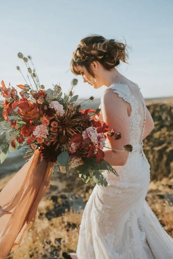 a moody lush bridal bouquet with rust, red, burgundy, pink blooms and textural greenery and colored ribbons