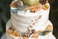 a naked wedding cake with caramel drip, gold leaf, cinnamon sticks, pinecones, greenery and a pear is a lovely idea for a fall or winter wedding