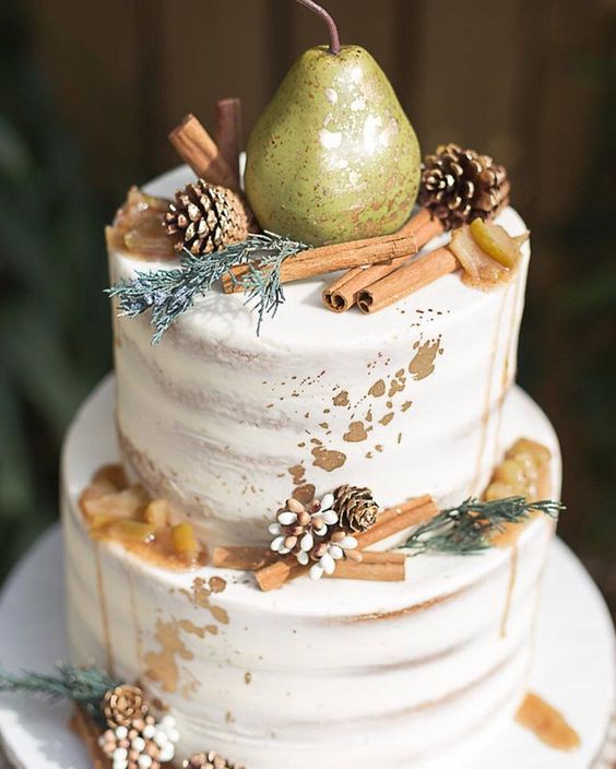 a naked wedding cake with caramel drip, gold leaf, cinnamon sticks, pinecones, greenery and a pear is a lovely idea for a fall or winter wedding