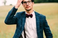 a navy groom plaid suit, a white shirt, black suspenders, a burgundy bow tie and black frame glasses are an awesome combo