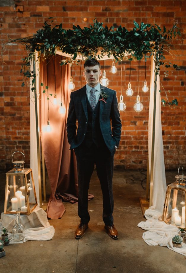 a navy windowpane print three-piece suit, a white shirt, a printed tie and brown shoes for a vintage-inspired groom's look