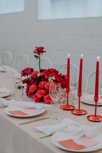 a neutral wedding tablescape with a tan tablecloth, white napkins, two-tone menues and a lush red floral centerpiece plus bold red candles