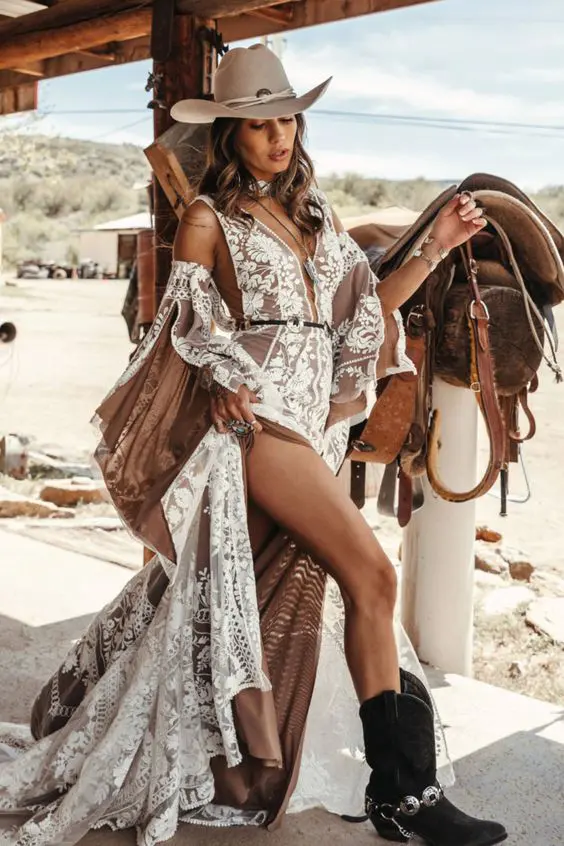 a nude and white boho lace A-line wedding dress with bell sleeves, a grey hat, black cowboy boots and pretty boho accessories for a boho bridal outfit