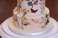 a painted wedding cake with flowers, laves, branches and butterflies is a lovely and bold idea to go for, looks amazing