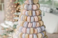 a pastel macaron tower with blush, blue and tan macarons, a purple bloom and greenery plus berries is a chic idea
