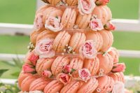 a pink macaron tower with a clear stand, light pink blooms and neutral ones is a beautiful idea for a pastel wedding