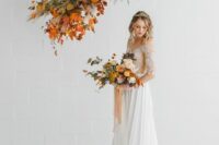 a pretty and cool fall wedding arrangement of bright leaves and greenery, blush and orange blooms and pampa sgrass for a fall wedding altar