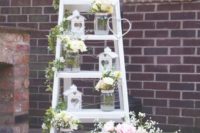 a pretty rustic wedding decoration of a white ladder, white blooms and greenery, white candle houses