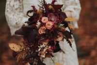 a refined dark cascading wedding bouquet of blush and plum-colored blooms, bold yellow leaves, feathers and gilded foliage is wow