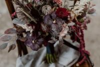 a refined dark wedding bouquet done with dark plum, hot pink and pink flowers, colored leaves and herbs for a boho wedding