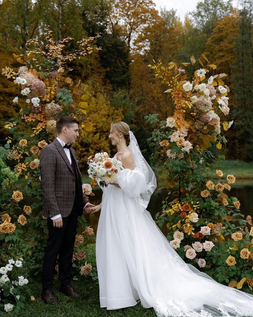 a refined fall wedding arch covered with greenery, blush, white and rust roses and bold fall leaves is wow