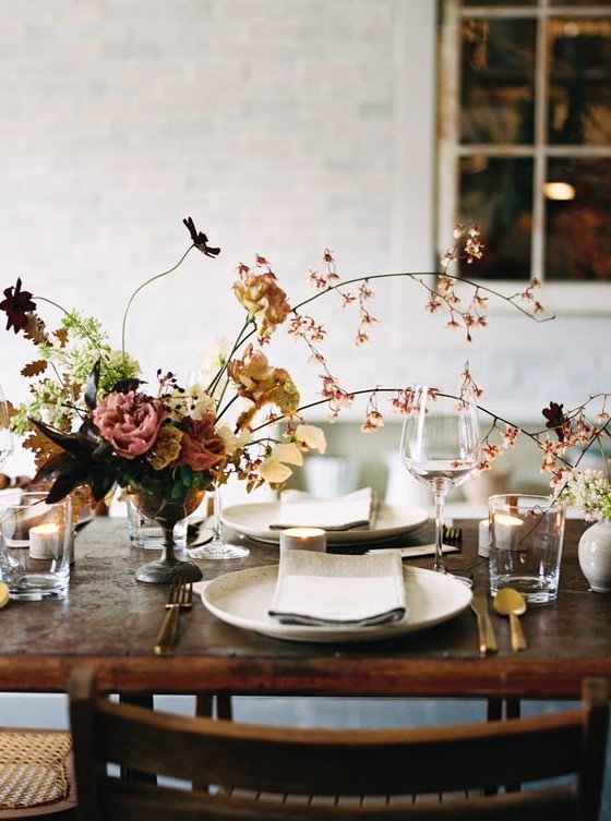 a refined fall wedding centerpiece of a bowl, greenery and foliage, blooming branches and dark blooms