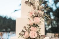 a refined wedding cake in white decorated with greenery, blush roses, grey butterflies is a chic and stylish idea