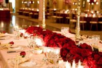 a refined wedding tablescape done with red roses on stands and on the table, gold touches and a blush tablecloth for more elegance