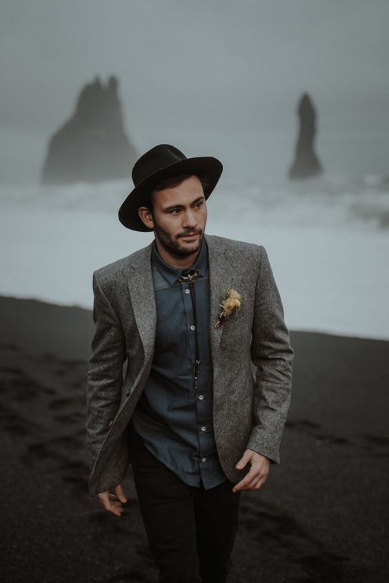 a relaxed groom's look with a grey jacket, a slate grey shirt, black pants, a black hat plus a bolo tie