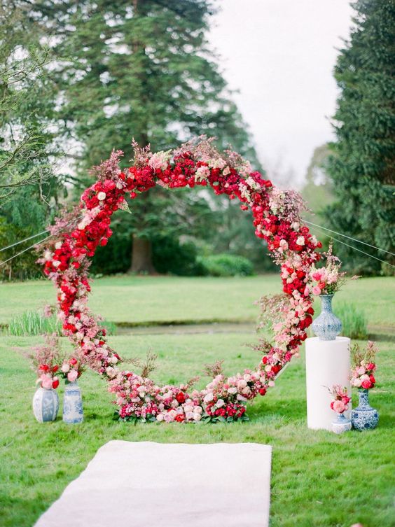 a round red and blush wedding arch with some blooming branches and vases with blooms is a gorgeous idea for a wedding