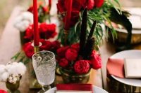 a rustic winter wedding tablescape with wood slices, red blooms, candles and napkins, greenery and cotton