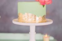 a small mint green wedding cake with gold leaf and a large pink bloom on top