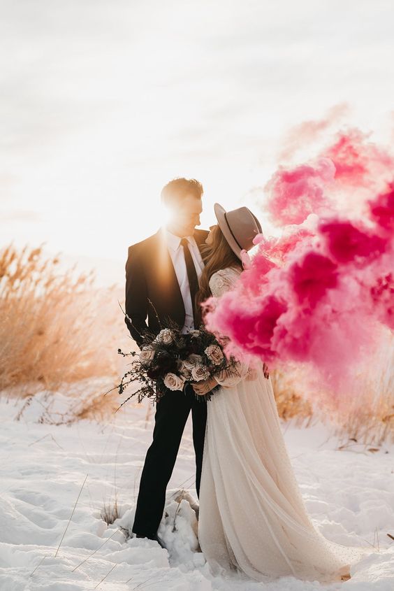 a snowy wedding portrait done with sunshine and pink smoke is amazing and makes the couple stand out a lot
