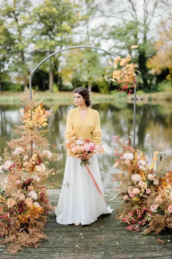 a sophisticated modern wedding arch with bright fall leaves, blush, white and mustard blooms and a gorgeous lake view is wow