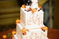 a square white buttercream wedding cake with patterns, sugar pumpkins and leaves plus pumpkin cake toppers
