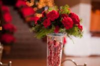 a tall vase with berries, red blooms and fir is a stylish and easy rustic centerpiece for a winter or Christmas wedding