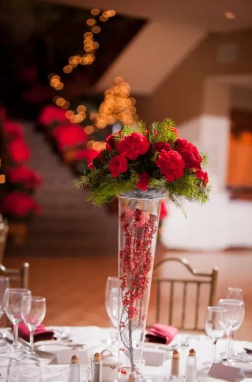 a tall vase with berries, red blooms and fir is a stylish and easy rustic centerpiece for a winter or Christmas wedding