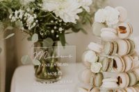 a very cool neutral and green macaron tower on a clear stand, with white blooms is a very chic and cool solution for a modern neutral wedding