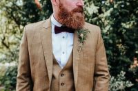 a vintage-inspired groom’s look with a beige three-piece pantsuit, a white shirt, a burgundy bow tie and a boutonniere