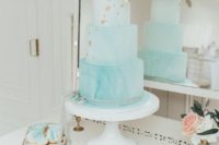a watercolor tiffany blue wedding cake decorated with gold foil and a large white sugar bloom on top