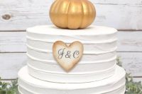 a white buttercream wedding cake with a faux gold pumpkin on top and a monogram cookie is a lovely idea for a rustic wedding