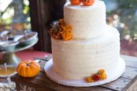 a white buttercream wedding cake with bright blooms and small edible pumpkins on top that act as cake toppers