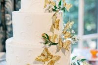 a white patterned cake with greenery and gold butterflies and baby’s breath is very beautiful and natural