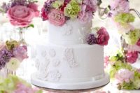 a white wedding cake decorated with flowers and butterflies plus pink and lilac blooms and greenery on top