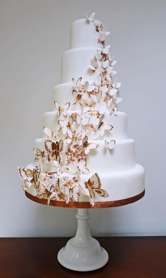 a white wedding cake decorated with painted amber blooms and with lots of butterflies climbing up the cake is wow