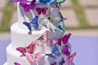a white wedding cake decorated with purple, green, white and pink butterflies looks very chic and very eye-catchy