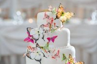 a white wedding cake decorated with yellow, pink and white butterflies looks spectacular and very bold and catches an eye