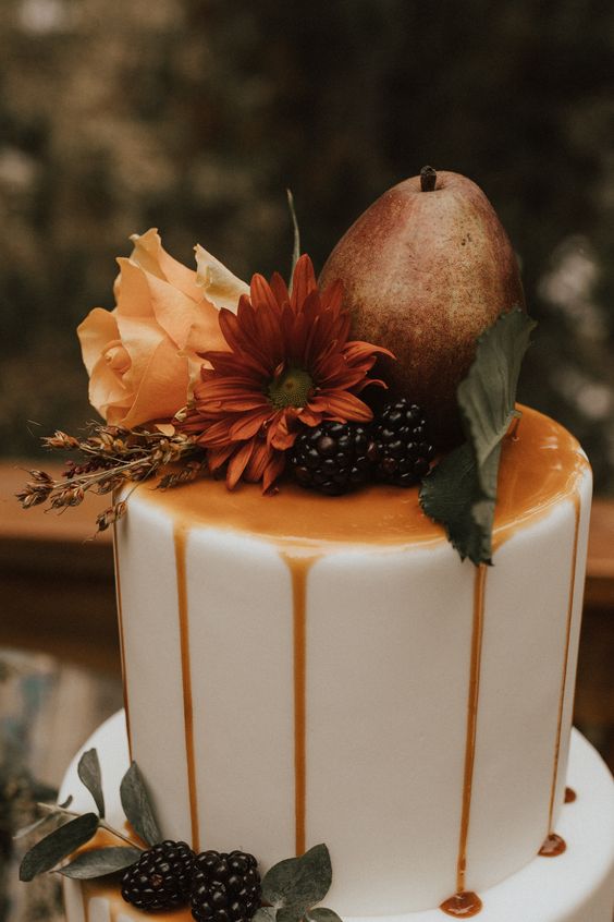 a white wedding cake with caramel drip, bold fall blooms, foliage and blackberries plus a pear on top is a lovely idea for a fall wedding