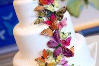 a white wedding cake with lots of colorful butterflies is a bold and cool idea of a wedding dessert to rock