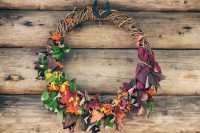 a wine wreath covered with greenery, dark foliage, berries and bright leaves is an all-natural fall wedding idea